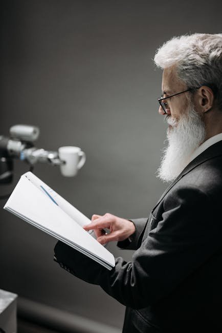 A scientist observes a robotic device while holding documentation in a lab.
